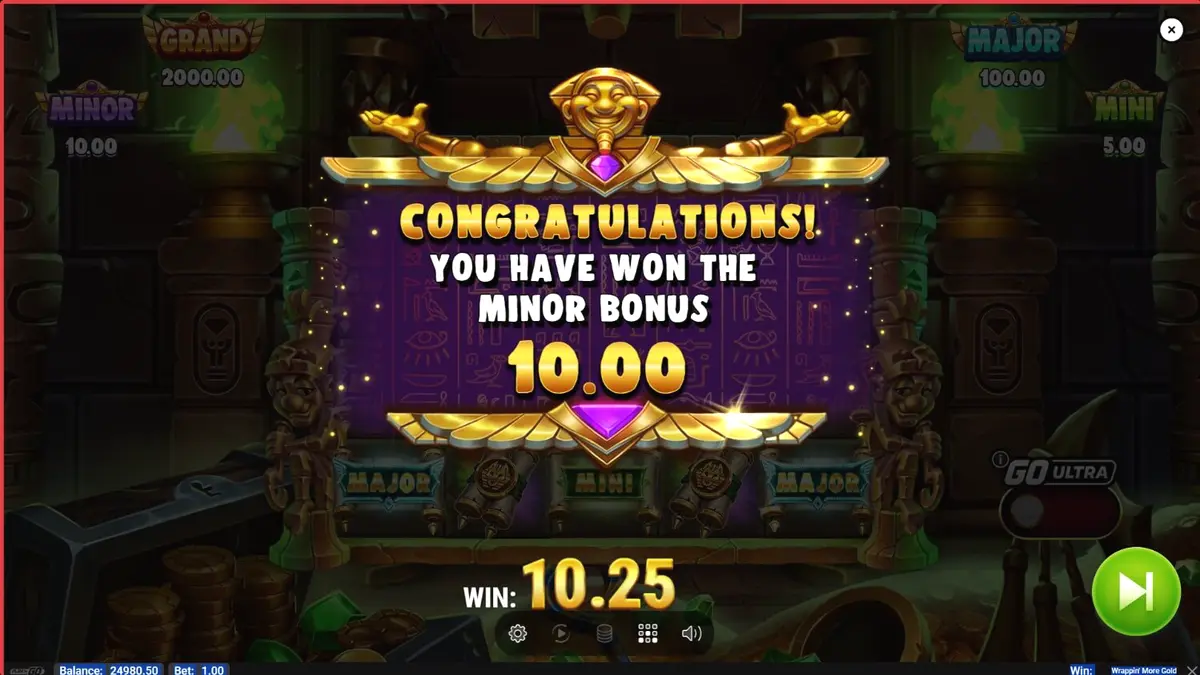 Mumi ramah dalam slot Wrappin’ More Gold dengan latar belakang harta karun Mesir.